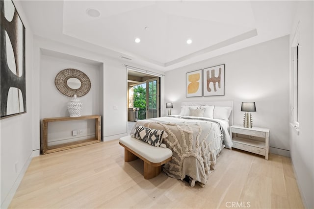 bedroom with light hardwood / wood-style floors and a tray ceiling