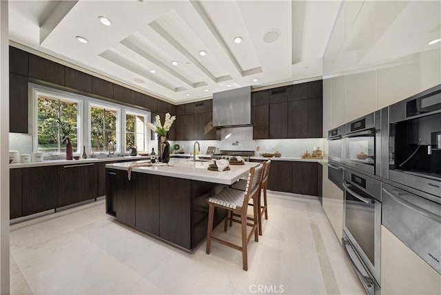 kitchen with a raised ceiling, decorative backsplash, a kitchen bar, and a center island with sink