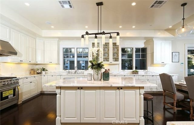 kitchen featuring high end stove, a center island, hanging light fixtures, white cabinets, and light stone counters