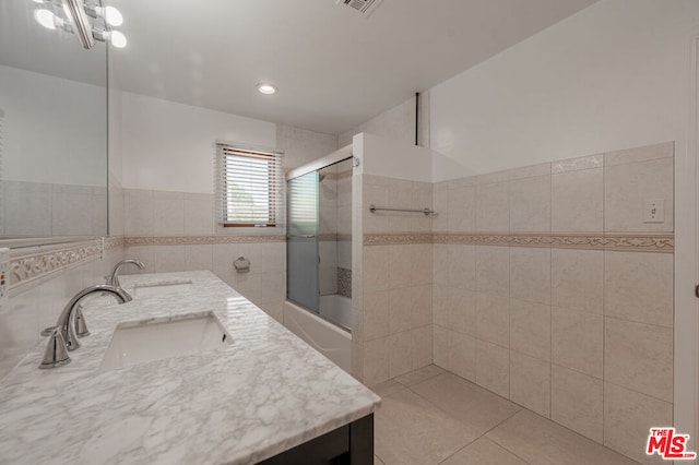 bathroom featuring tile patterned floors, vanity, shower / bath combination with glass door, and tile walls