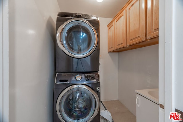 clothes washing area with cabinets, light tile patterned floors, and stacked washer and dryer