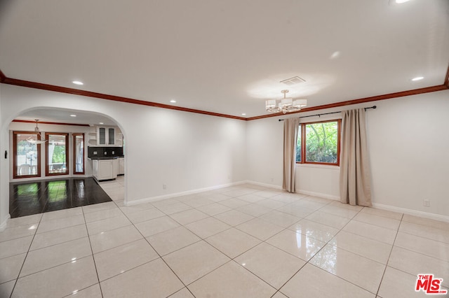 spare room with crown molding, a notable chandelier, and light tile patterned flooring