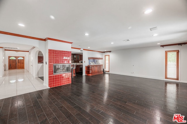 unfurnished living room with wood-type flooring, crown molding, and a tiled fireplace