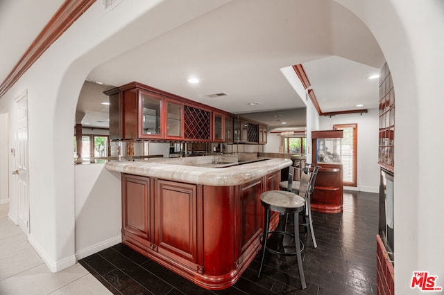 kitchen featuring a kitchen breakfast bar, crown molding, dark hardwood / wood-style flooring, light stone counters, and kitchen peninsula