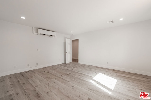 unfurnished room with a wall unit AC and light hardwood / wood-style floors