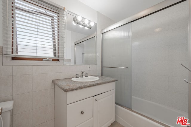 full bathroom featuring combined bath / shower with glass door, decorative backsplash, vanity, tile walls, and toilet