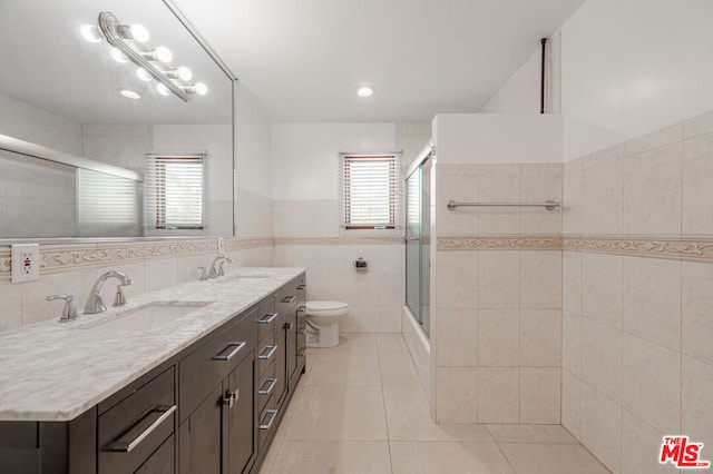 full bathroom with combined bath / shower with glass door, tile patterned floors, toilet, vanity, and tile walls