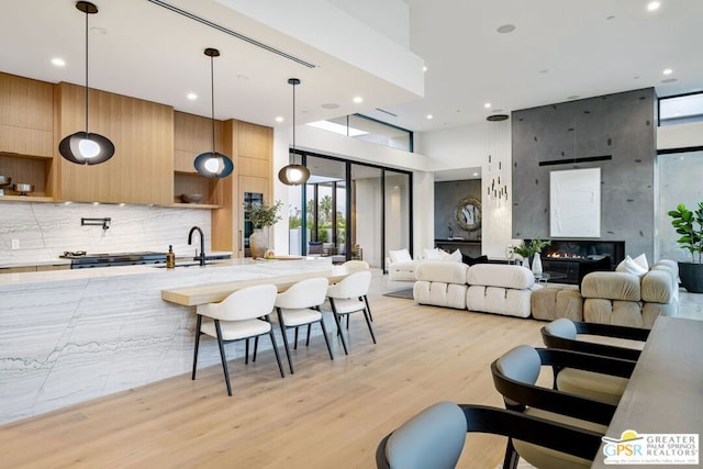 kitchen featuring a towering ceiling, a fireplace, light hardwood / wood-style floors, decorative light fixtures, and decorative backsplash