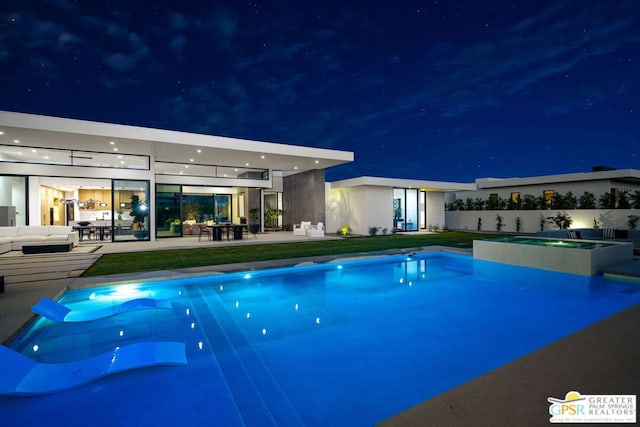 pool at twilight with a patio and an in ground hot tub