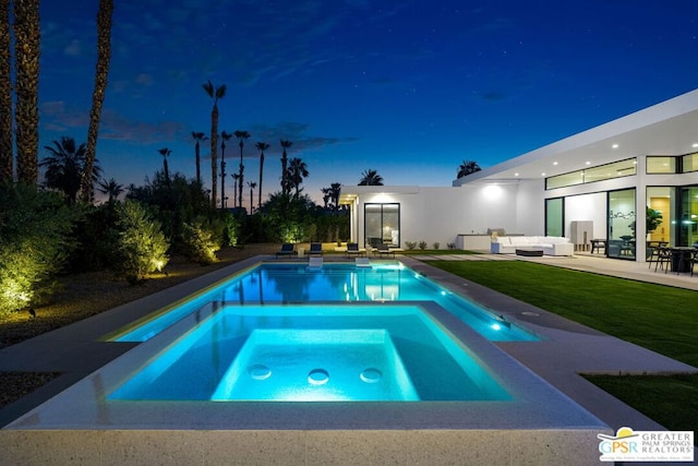 pool at night featuring a yard, a patio area, an in ground hot tub, and an outdoor hangout area