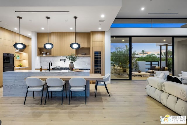 kitchen with sink, backsplash, decorative light fixtures, light hardwood / wood-style flooring, and a kitchen island with sink