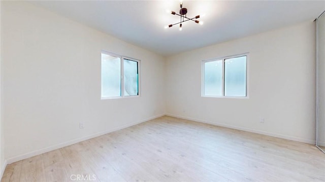 spare room featuring a chandelier, light wood-type flooring, and baseboards