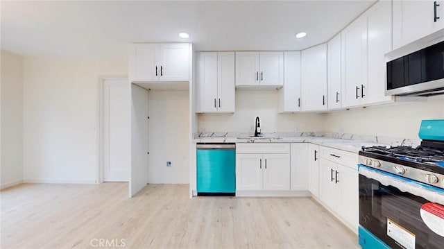 kitchen with stainless steel appliances, light wood-style floors, a sink, and white cabinets