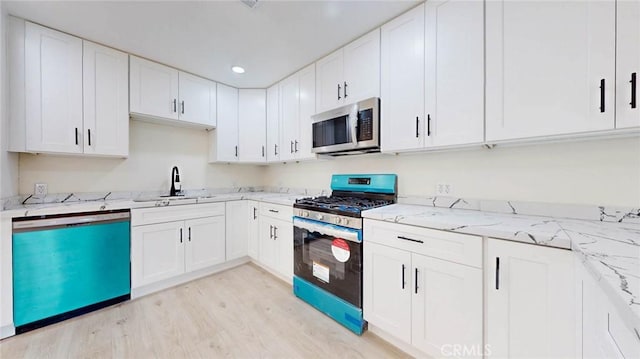 kitchen with appliances with stainless steel finishes, white cabinetry, a sink, and light wood-style flooring