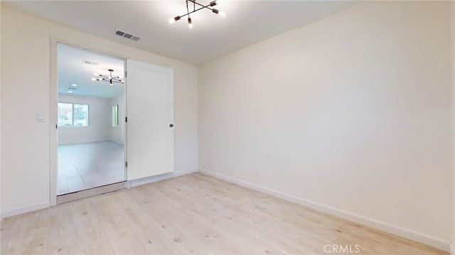 empty room featuring light wood-style floors, baseboards, visible vents, and a chandelier