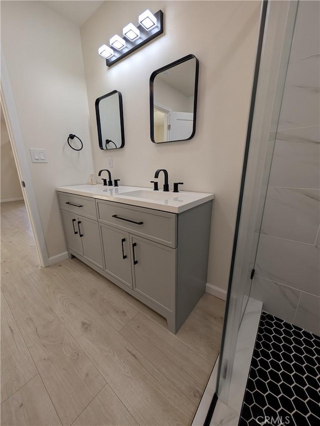 bathroom with wood finished floors, a sink, baseboards, a shower stall, and double vanity