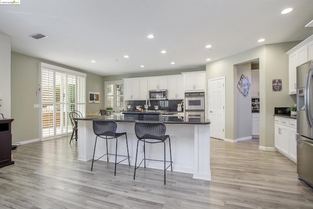 kitchen featuring white cabinetry, light hardwood / wood-style flooring, a kitchen breakfast bar, an island with sink, and stainless steel appliances