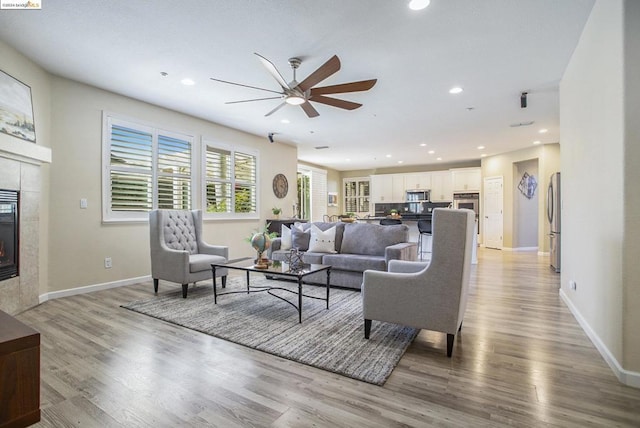 living room with ceiling fan, a fireplace, and light hardwood / wood-style flooring