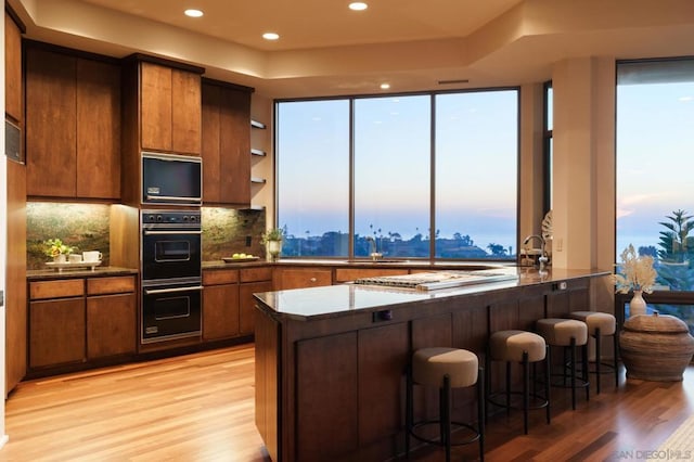 kitchen featuring kitchen peninsula, backsplash, a kitchen bar, black double oven, and light hardwood / wood-style floors