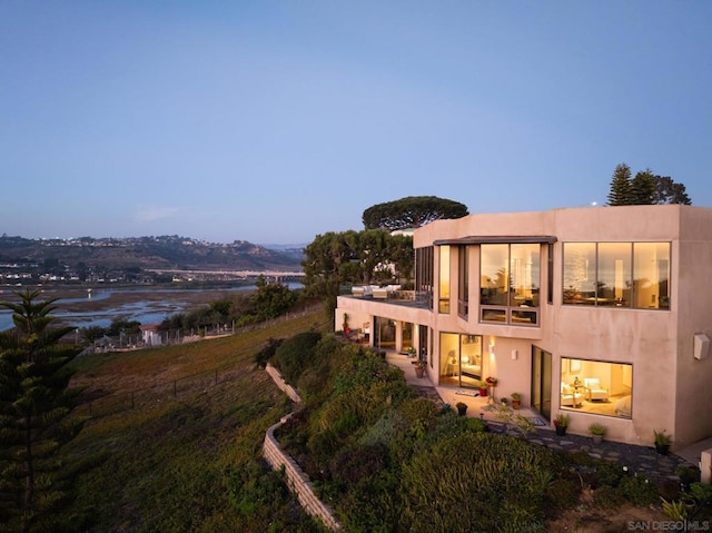 back house at dusk featuring a water view and a patio area