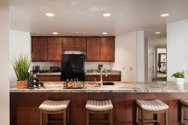 kitchen featuring a breakfast bar area, black refrigerator, kitchen peninsula, sink, and light stone counters