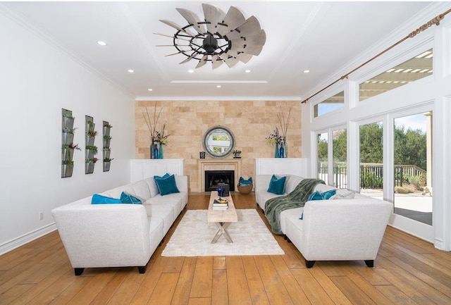 living room with ceiling fan, a tray ceiling, ornamental molding, light hardwood / wood-style floors, and a tiled fireplace