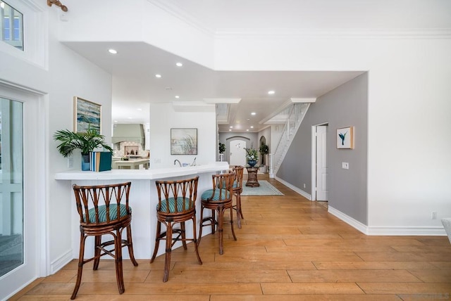 kitchen with ornamental molding, a kitchen bar, kitchen peninsula, and light hardwood / wood-style flooring