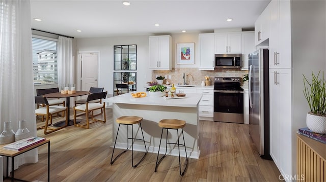 kitchen with sink, appliances with stainless steel finishes, decorative backsplash, white cabinets, and light wood-type flooring