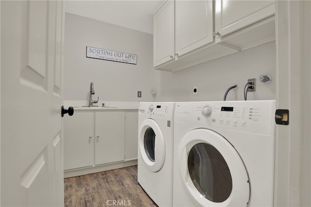 clothes washing area featuring a sink, cabinet space, wood finished floors, and washer and dryer