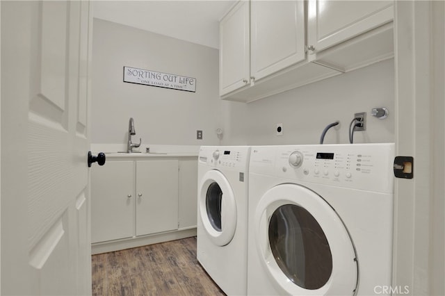 laundry room featuring wood finished floors, washing machine and clothes dryer, a sink, and cabinet space