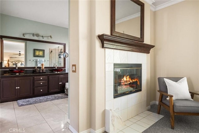 full bathroom featuring crown molding, double vanity, a tiled fireplace, and a sink