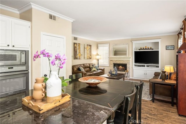 dining space featuring crown molding, a brick fireplace, visible vents, and dark wood-type flooring