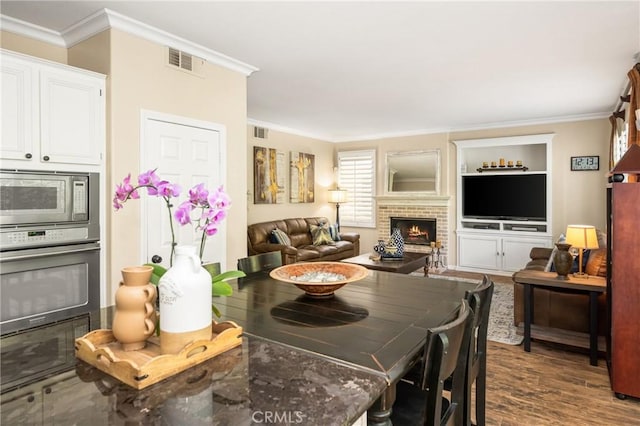 dining space featuring a fireplace, visible vents, ornamental molding, and dark wood finished floors