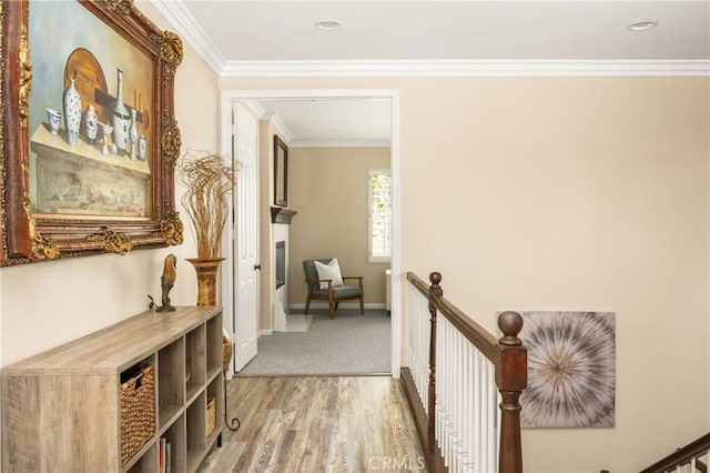 hallway with an upstairs landing, baseboards, crown molding, and wood finished floors