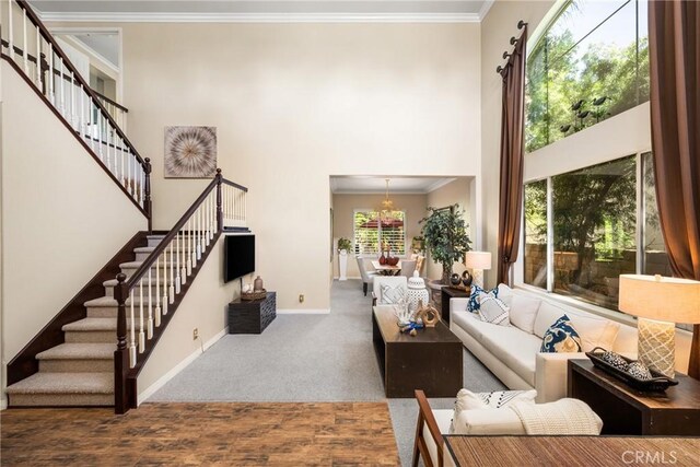 living room featuring stairway, a high ceiling, crown molding, baseboards, and a chandelier