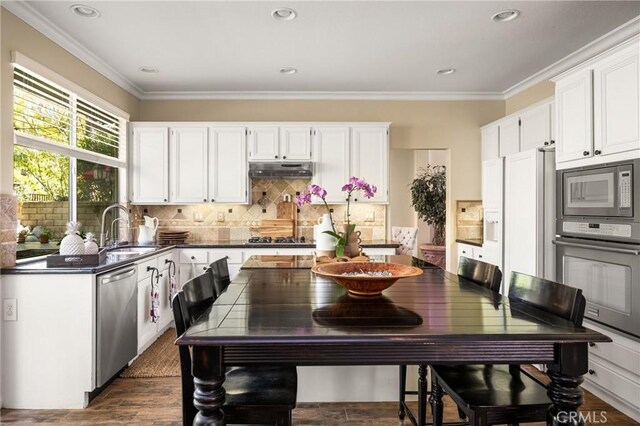 kitchen featuring dark countertops, crown molding, under cabinet range hood, appliances with stainless steel finishes, and a sink