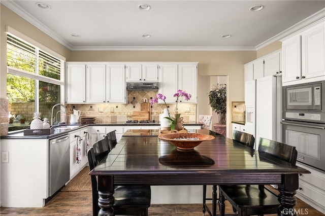 kitchen with dark countertops, white cabinets, under cabinet range hood, stainless steel appliances, and a sink