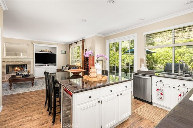 kitchen with ornamental molding, light wood-style flooring, wine cooler, stainless steel dishwasher, and a sink