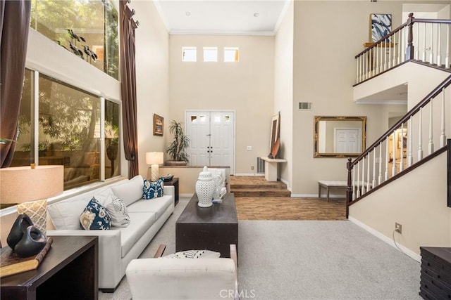 living room with stairway, baseboards, visible vents, a high ceiling, and ornamental molding