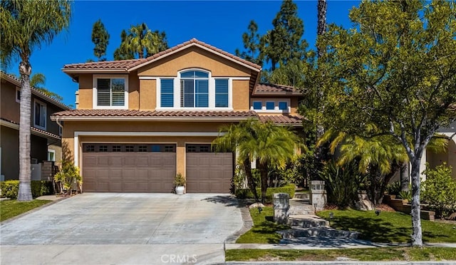 mediterranean / spanish house featuring a tiled roof, an attached garage, driveway, and stucco siding