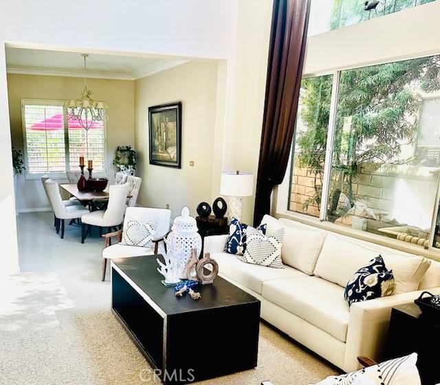 living room with carpet flooring, baseboards, an inviting chandelier, and ornamental molding