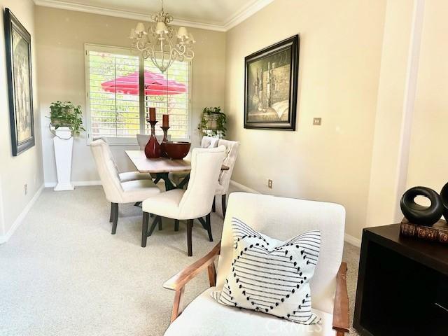 dining space with a chandelier, baseboards, ornamental molding, and carpet floors