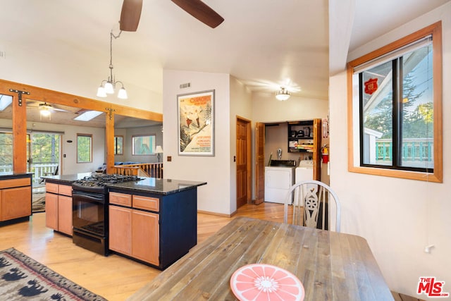 kitchen with black gas range, light wood-type flooring, washing machine and dryer, lofted ceiling with skylight, and a center island