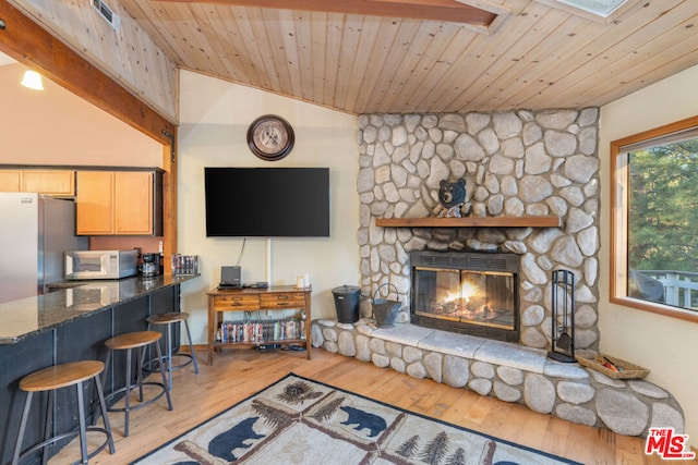 living room featuring lofted ceiling with skylight, a stone fireplace, light wood-type flooring, and wooden ceiling