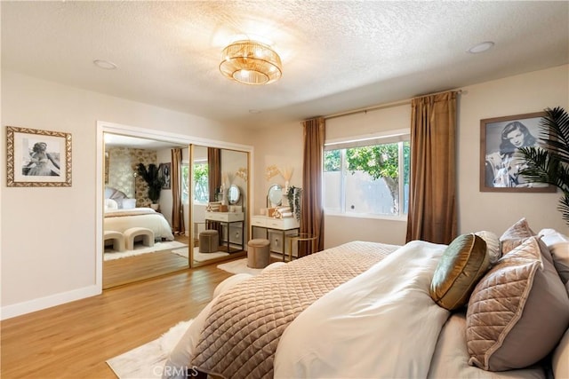 bedroom featuring a textured ceiling, a closet, light hardwood / wood-style flooring, and multiple windows