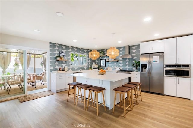 kitchen with white cabinetry, wall chimney exhaust hood, pendant lighting, appliances with stainless steel finishes, and light wood-type flooring