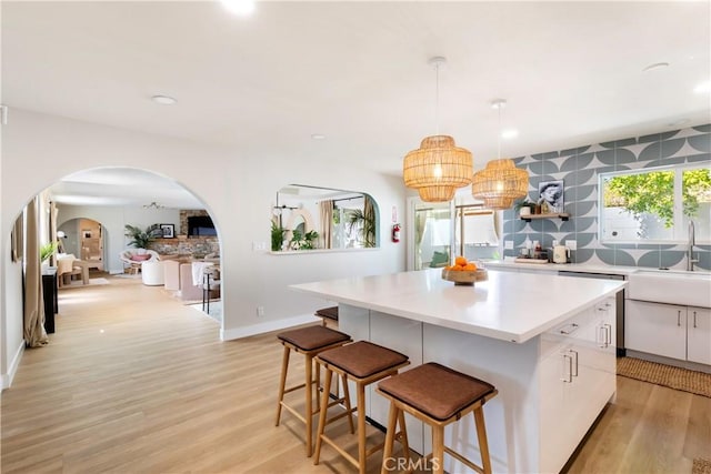 kitchen with a center island, sink, hanging light fixtures, light hardwood / wood-style flooring, and white cabinetry