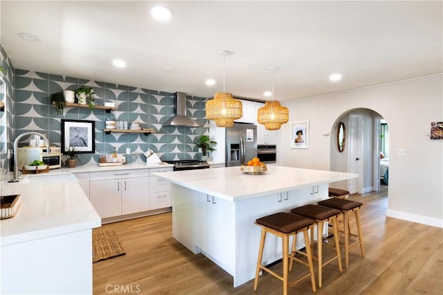 kitchen featuring a center island, wall chimney exhaust hood, stainless steel appliances, white cabinets, and light wood-type flooring