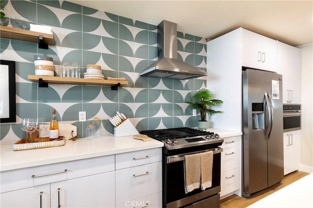 kitchen with white cabinetry, wall chimney exhaust hood, light hardwood / wood-style floors, decorative backsplash, and appliances with stainless steel finishes