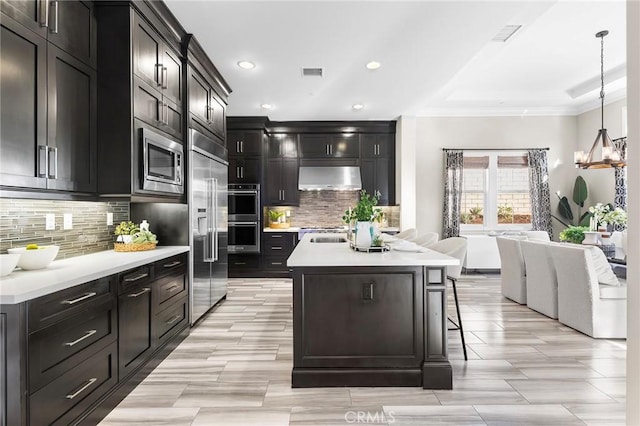 kitchen with pendant lighting, built in appliances, backsplash, and wall chimney range hood